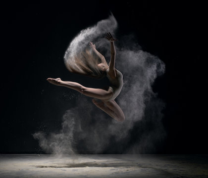 Girl in body jumps in dust cloud black background