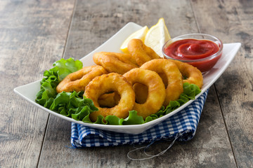 Fried calamari rings with lettuce and ketchup on wooden background

