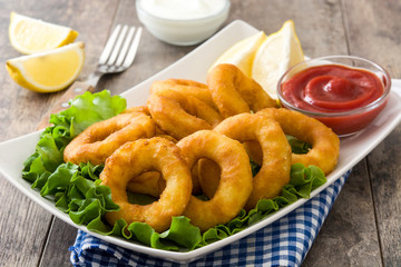 Fried calamari rings with lettuce and ketchup on wooden background
