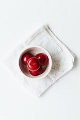 Small bowl of red plums on white vintage napkin