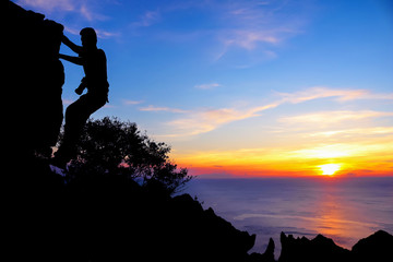 Photographer climbing rock on the mountain with a blue sky sunset 