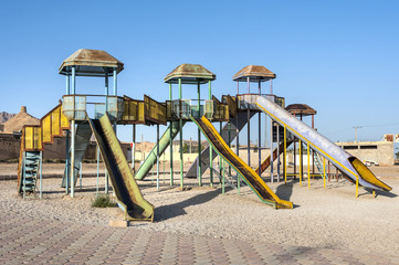 Fototapeta na wymiar Iran, Anarak: Empty playground with .metal climbing contraption, three slides and village center in the background