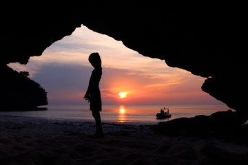 Girls stand in front of a cave on the beach at sunset. 
