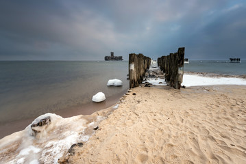 Frozen wooden breakwater at Baltic Sea in Babie Doly. The old torpedo station in background....