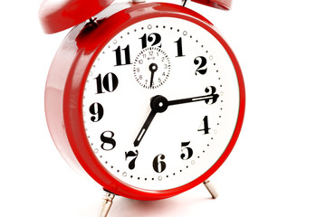 A quarter past seven on a round red alarm clock on white background - isolated