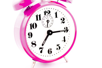 Round pink alarm clock on white background isolated. The image of the retro clock shows a quarter past seven.