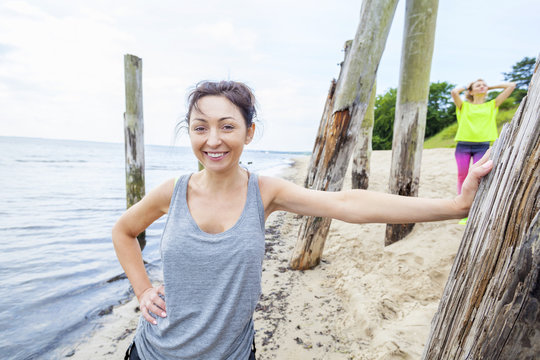 Woman in tank top on beach leaning against wooden post