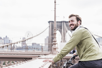 USA, New York City, smiling man on bicycle on Brooklyn Bridge