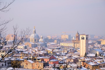 Fototapeta na wymiar View over the city rooftops with sunlight and snow. Brescia, Italy.