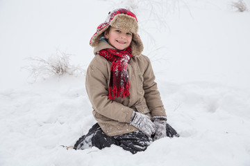 Fototapeta na wymiar Smiling boy in warm clothes sitting on snow