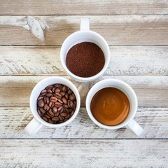 Three cups of coffee: beans, ground and brewed coffee on white wooded desk