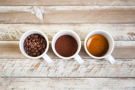 Three cups of coffee: beans, ground and brewed coffee in a row,  on white wooded table