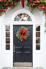 Beautiful black door decorated for Christmas with evergreen wreath, garland, and red bows