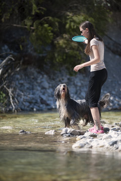 Woman and her dog walking in water. Dog is very wet and waiting her to trough him a toy, freesbee