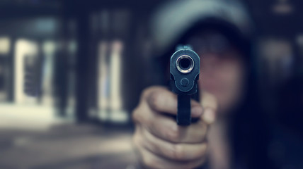 Woman pointing a gun at the target on dark background, selective focus