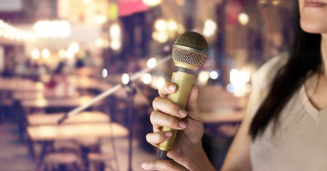 Woman holding microphone in hand on pub and restaurant background