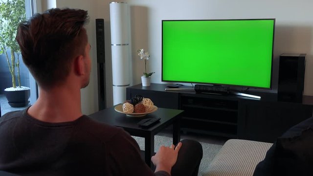 A man screams and gesticulates angrily at a TV with a green screen
