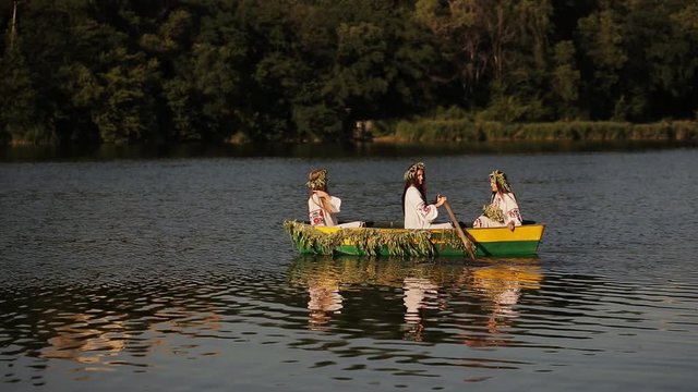 Three young girls with long hair in a boat floating on the river. Girls rowing oars on the water.