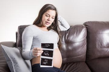 Pregnant woman looking at her baby's ultrasound scan in her living room