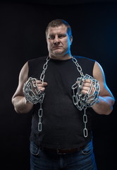 Actor Brutal man with a chain in his hands on a black background.