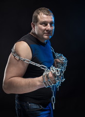 Actor Brutal man with a chain in his hands on a black background.