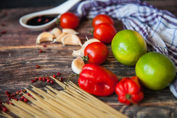 talian food background, with tomatoes, basil, spaghetti, mushrooms, parmesan, olive oil, sauce, lime, garlic, peppercorns, rosemary, thyme. Wooden background with fork