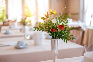 Vase with flowers and leaves. Blurred dining tables. Tasty food and calm atmosphere.