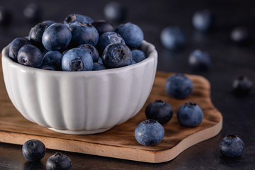 Juicy and fresh picked blueberry in whire bowl on rustic wooden board, selective focus