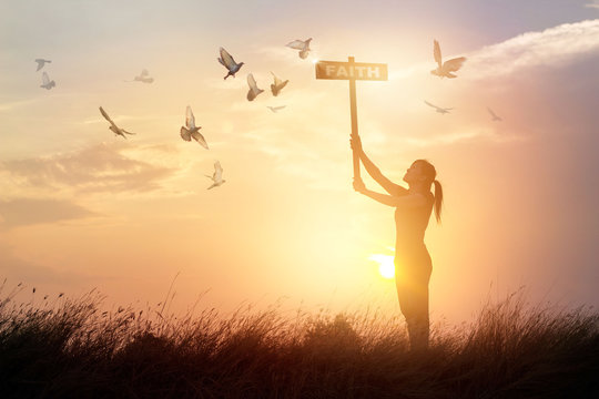 Woman holds a sign with word faith and flying birds on nature sunset