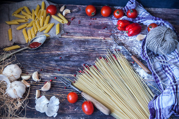 Italian food background, with tomatoes, basil, spaghetti, mushrooms, parmesan, olive oil, sauce, lime, garlic, peppercorns, rosemary, thyme. Wooden background with fork