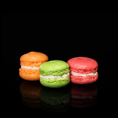 Multicolored macaroons isolated on black background with reflection. Free space for text