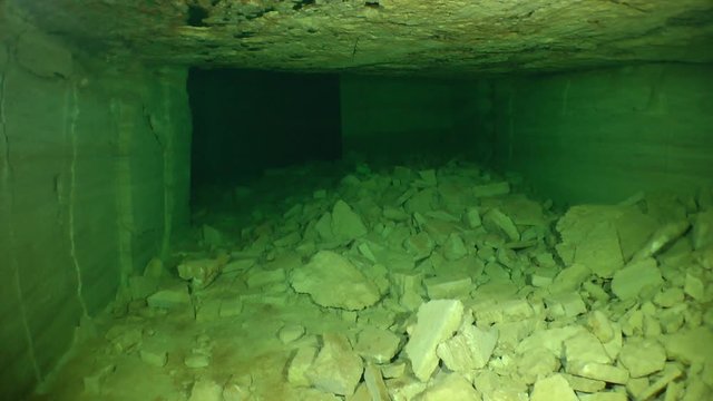The movement of camera in a wide half-buried by stone corridor of flooded catacombs.

