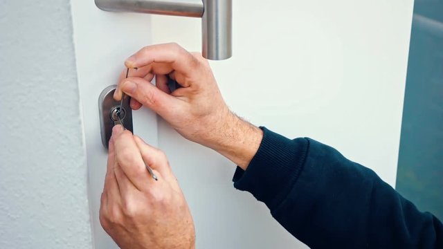 Intruder or Burglar with lockpick tool opens the front door to enter the house. could also be used for key service or locksmith concept