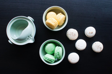 Cup of tea with french macaroon on dark background. Tea pot, cup of tea, color macaroon lying on black background.