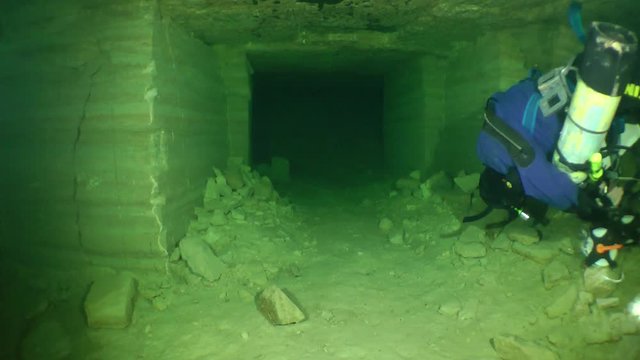 Speleologist unwinds a tape measure swims along the corridor of flooded mine.

