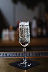 A glass of sparkling wine with berries inside, on the bar stand. Selective focus, small depth of field, film grain effect.