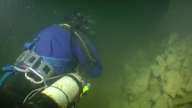 Speleologist swims along the corridor of flooded mine twisting a tape measure.

