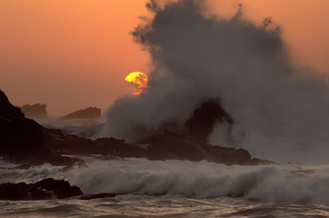 Fototapeta na wymiar wave wildly crashing on a rock while the sun sets