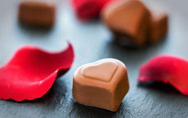 Pralinen in Herzform mir Rosenblättern auf schwarzem Schiefer Hintergrund