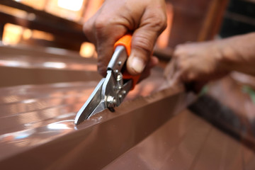 Workers use scissors to cut the metal sheet for roofing.  - obrazy, fototapety, plakaty