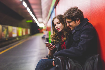 Young beautiful couple in love using smart phone together in the subway - interaction, love, technology concept