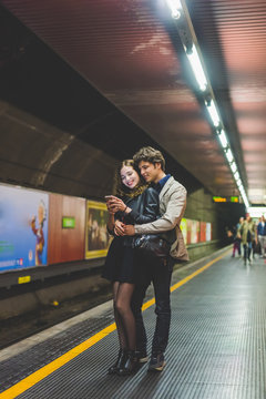 Young beautiful couple in love hugging using smart phone together in the subway - interaction, love, technology concept