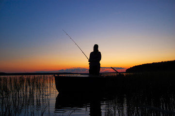 A fisherwoman with a fishing rod standing in boat 