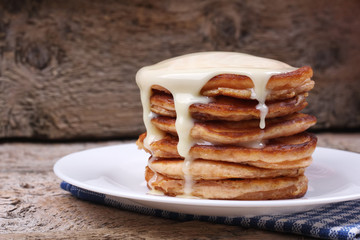 Stack of pancakes with milky sauce on the wooden table in the kitchen. A lot of tasty pancakes.