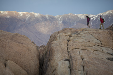 A man and woman hiking on huge boulders in the Sierra Nevada Mountains, near Lone Pine, California.