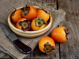 Delicious ripe orange persimmons in bowl on wooden background. Selective focus