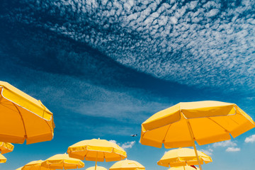 Several yellow umbrellas on the beach against blue sky with clou