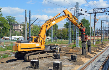 Экскаватор устанавливает сваю для новой платформы железнодорожной станции 