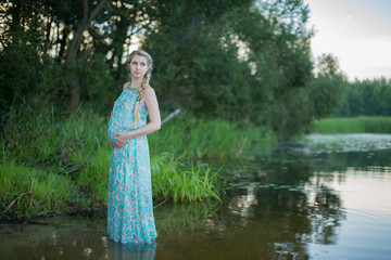 Беременная девушка в платье стоит в реке