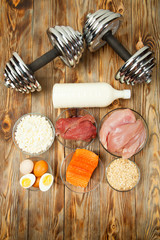 Fototapeta na wymiar Protein, fish, cheese, eggs, meat, chicken and dumbbells on a wooden background